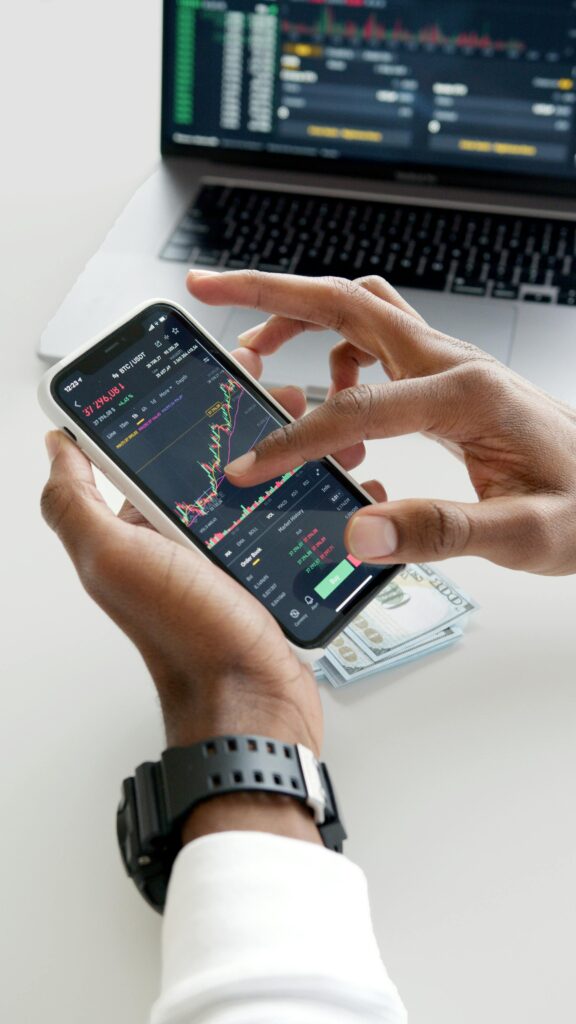 Hands using smartphone trading app with charts, dollar bills in background.